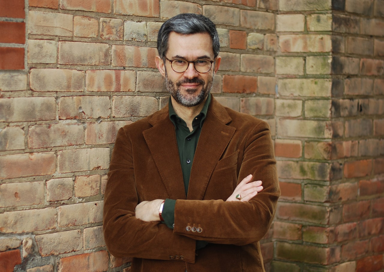 Pedro Mendes in a brown jacket in front of a wall