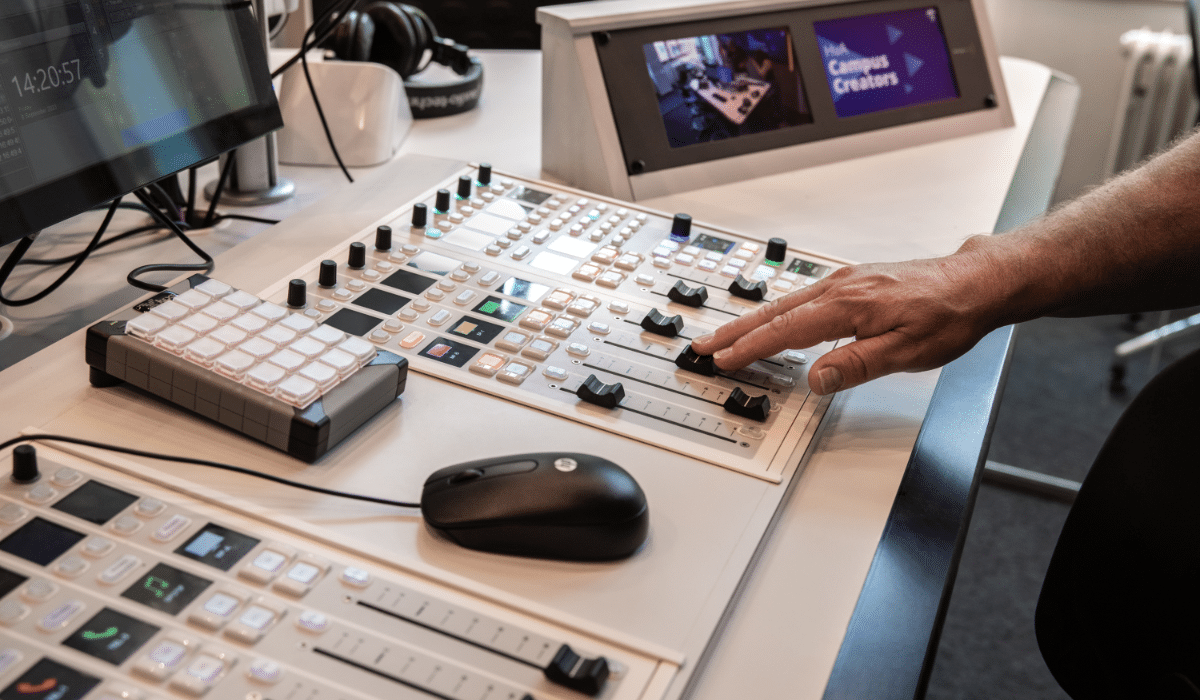A hand adjusting a fader on a radio mixing console