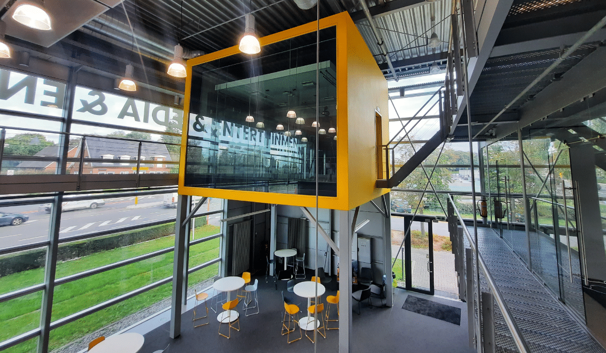 An elevated orange box with a wall made of glass which houses a radio studio
