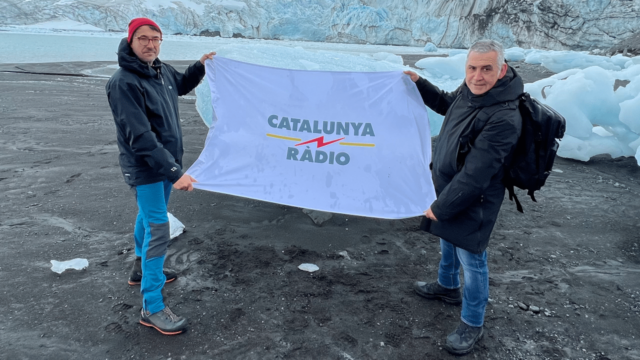 Two engineers from Catalunya Ràdio hold a flag with the radio station's name in Antarctica