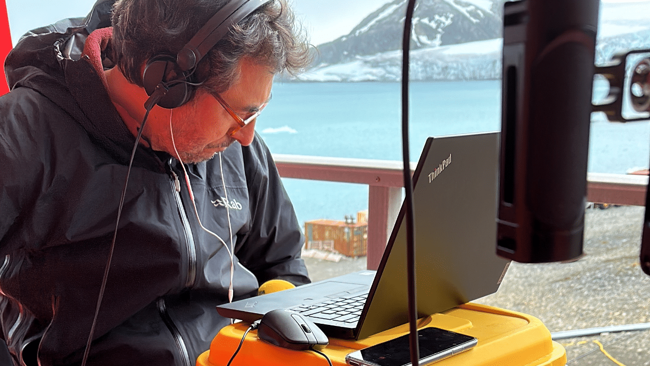 An engineer from Catalunya Ràdio working on a laptop in Antarctica with remote and snowy mountains In the background